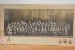 A large black and white photograph of an orchestra, c. 1900, the musicians set against an imposing