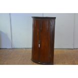 A George III inlaid mahogany hanging corner cupboard, bowfronted, with moulded cornice above a