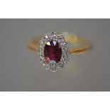 A ruby and diamond cluster ring, the oval-cut ruby within a band of round brilliant-cut diamonds,