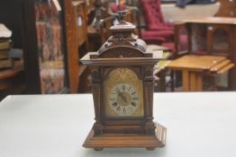 An Edwardian walnut bracket style mantle clock with pedimented top above an arched glazed panel door