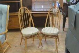 A pair of Ercol arched spindle back light elm dining chairs with shaped wood seats on splay supports