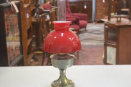 A brass Victorian style oil lamp with red cased glass shade, complete with funnel, converted to