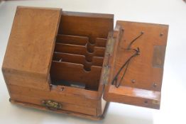 An Edwardian oak slope top stationery rack with twin fold out panel doors enclosing a fitted