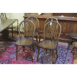 A set of four Windsor style spindle back dining chairs with shaped wood seats, raised on turned