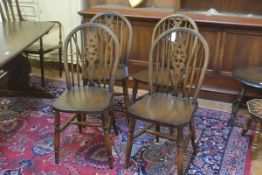 A set of four Windsor style spindle back dining chairs with shaped wood seats, raised on turned