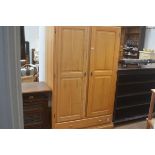 A laminated pine upright wardrobe, the plain top above a pair of fielded panel doors enclosing a