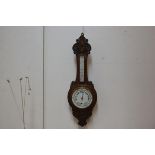 An Edwardian carved oak aneroid barometer and thermometer with enamelled dial. 90cm by 30cm