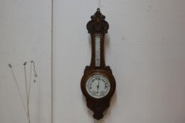 An Edwardian carved oak aneroid barometer and thermometer with enamelled dial. 90cm by 30cm