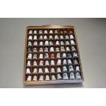 A wall display stand containing a collection of sixty nine ceramic and three metal thimbles (25cm