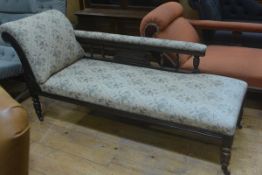 An Edwardian walnut chaise longue with scroll end and baluster support backrest, upholstered in