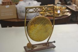 An Edwardian brass dinner gong, raised on pierced curved stand and oak base, complete with felt