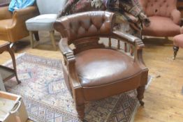 An Edwardian walnut framed horseshoe back tub chair upholstered in brown hide, with relief carved