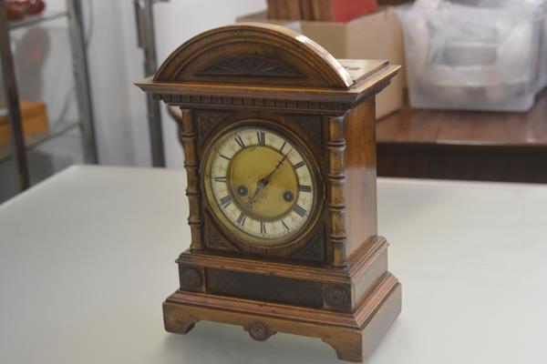 An Edwardian walnut mantle clock with arched top above an enamelled dial with twin key apertures and