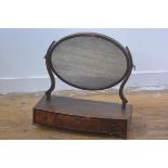 A 19thc mahogany swing mirror, the oval mirror raised on scroll end supports and bow fronted base,