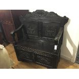 A late Victorian carved oak hall settle, the panelled back with shell and scroll carved crest, the