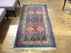 A Caucasian style rug, with twin diamond shaped panels enclosed within stylised leaf and