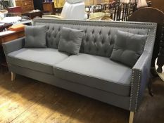 A stylish modern three seater sofa upholstered in grey linen with button upholstered back and