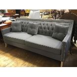 A stylish modern three seater sofa upholstered in grey linen with button upholstered back and