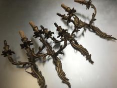 A set of four Louis XV style gilt metal two light wall sconces, each with leaf cast scrolling back