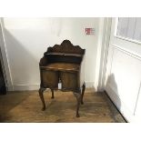 A figured walnut bedside with scalloped top and open shelf above two panel doors, raised on carved