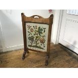 An Arts & Crafts oak firescreen with arched centre handle to top enclosing a glazed crewel work