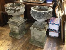 A pair of composition circular stone urns with swags and associated pedestals with laurel wreaths,