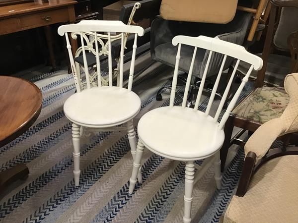 A pair of white painted spindle back kitchen chairs with circular shaped seats, on ring turned