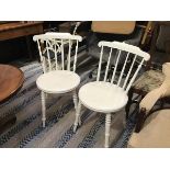 A pair of white painted spindle back kitchen chairs with circular shaped seats, on ring turned