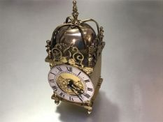 A modern reproduction brass lantern style clock with silvered dial and roman numerals, raised on bun