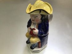 A 19thc Staffordshire seated Toby jug, with yellow tricorn hat, decorated with polychrome enamels (