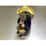 A 19thc Staffordshire seated Toby jug, with yellow tricorn hat, decorated with polychrome enamels (