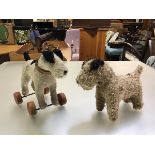 A mohair wool straw filled terrier on wheels and another similar, with inset glass bead eyes (h.24cm