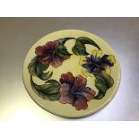 A Moorcroft circular dish with lily pattern border, with tubelined leaves and flowers, yellow
