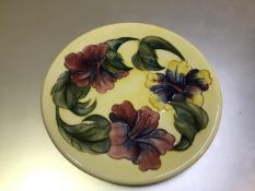 A Moorcroft circular dish with lily pattern border, with tubelined leaves and flowers, yellow