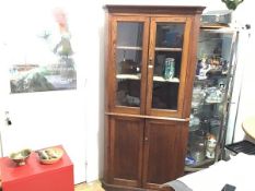 An Edwardian oak double corner cupboard with moulded dentil cornice above a pair of glazed panel