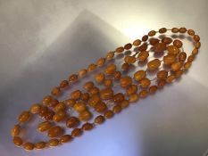 A long strand of graduated "butterscotch" amber beads, c. 1920, of shaped oval form, forty-one beads