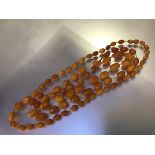 A long strand of graduated "butterscotch" amber beads, c. 1920, of shaped oval form, forty-one beads