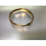 An Edwardian 9ct gold "buckle" bangle, the hinged front with buckle motif on engraved scrollwork,