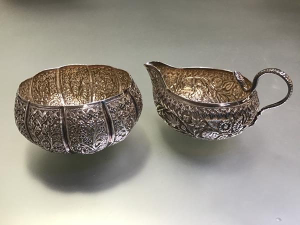 An Indian white metal cream and sugar bowl, c. 1900, each finely chased with flowers and foliage,