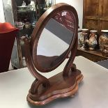 A Victorian mahogany toilet mirror, the oval plate within a cushion moulded frame between scroll