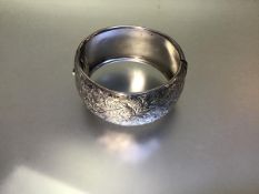 A substantial late Victorian silver cuff bangle, hinged, hollow, engraved with foliate scrollwork,