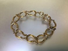 A 9ct gold horseshoe link bracelet, c. 1900, each horseshoe joined by chains, stamped mark. Length