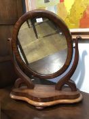 A Victorian mahogany toilet mirror, the oval plate within a cushion moulded frame between scroll