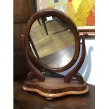 A Victorian mahogany toilet mirror, the oval plate within a cushion moulded frame between scroll