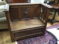 An Edwardian carved oak settle, the panel back enclosed by turned pilasters, above a hinged seat,