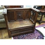 An Edwardian carved oak settle, the panel back enclosed by turned pilasters, above a hinged seat,