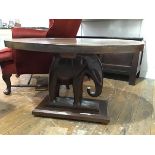A South Asian oval coffee table, the plain top resting on a carved elephant on stepped block base (