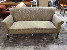 An Edwardian mahogany framed three seater sofa upholstered in floral moquette raised on tapered legs