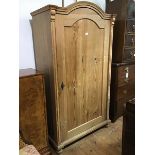 A Continental pitch pine Armoire, the arched top above a panel door, with plain sides, on moulded