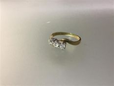 A three stone diamond ring, the round brilliant-cut stones claw-set on a crossover yellow metal band
